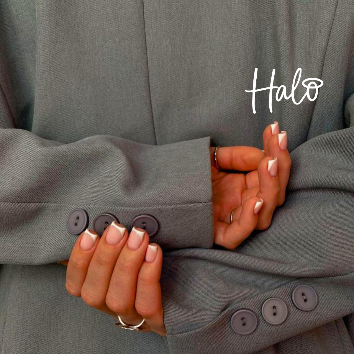 Close-up of white French tip nails with a modern square shape on natural nails, photographed against a grey blazer.