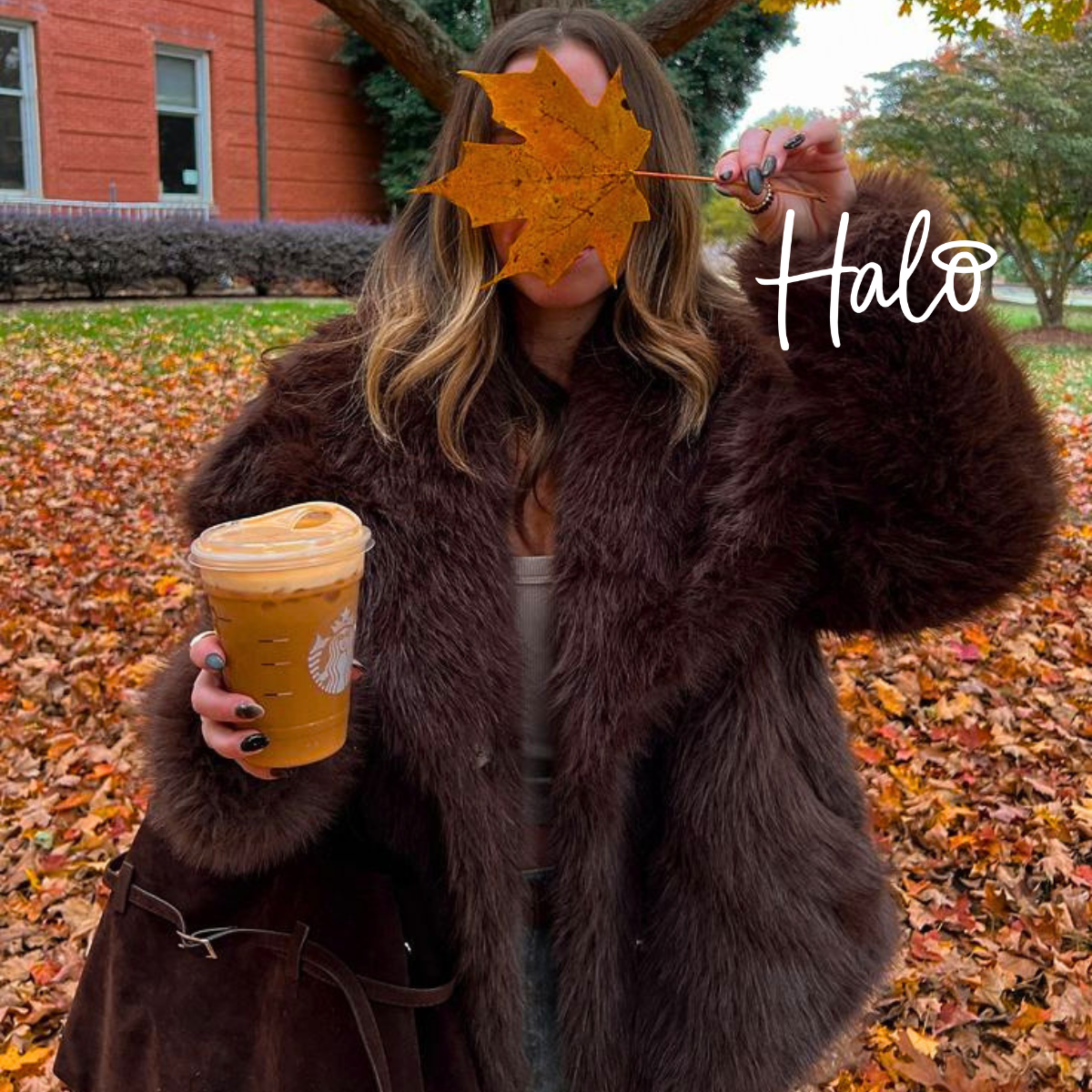 **Alt text:** Woman holding an autumn leaf and iced coffee, showing a dark Halo manicure against a backdrop of fallen autumn leaves.