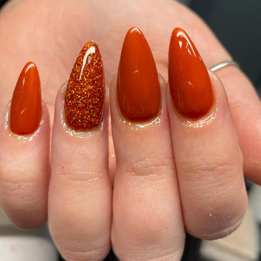 Stiletto nails in orange nail colour with glitter on one nail