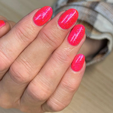 Close-up of a hand with bright pink nail polish on a blurred background