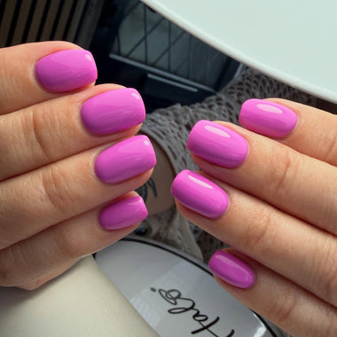 Close-up of hands with pink nail polish holding a nail polish bottle.