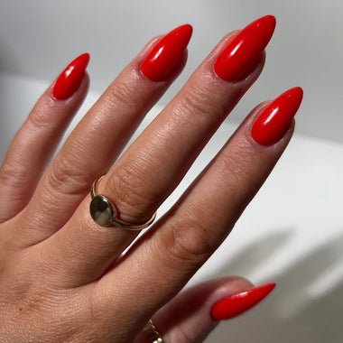 Hand with red nails and a gold ring on a neutral background