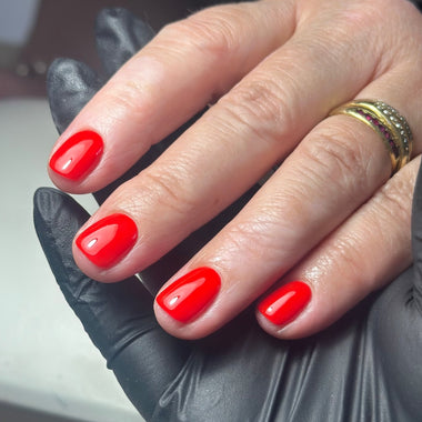Hand with red nail polish wearing a gold ring, against a neutral background