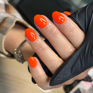 Hand with bright orange nails wearing a black glove, blurred background