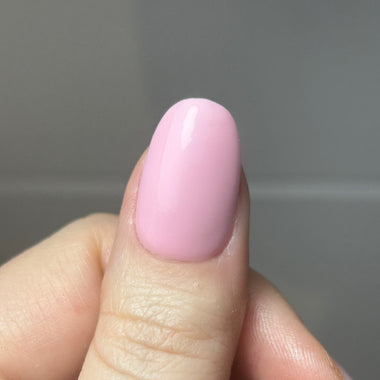 Close-up of a hand with a pink nail against a neutral background