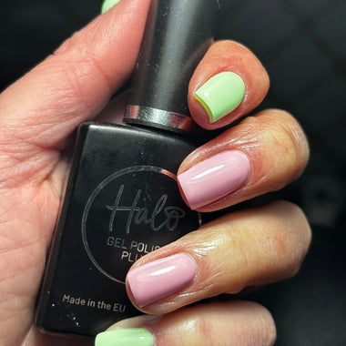 Hand holding a black nail polish bottle with green and pink nails