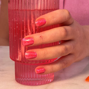 Hand holding a pink ribbed glass with pink nail polish against a blurred background