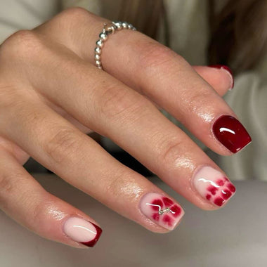 Hand with red and white floral nail design on a neutral background
