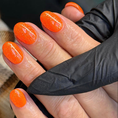 Hand with orange nail polish wearing a black glove against a blurred background