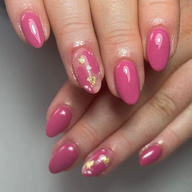 Close-up of a hand with pink nails and gold heart decorations on a neutral background