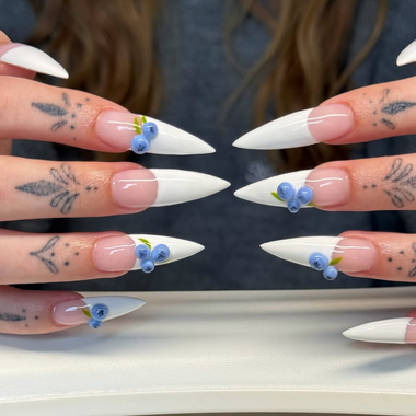 Close-up of hands with white nail polish and blue decorative elements, set against a blurred background.
