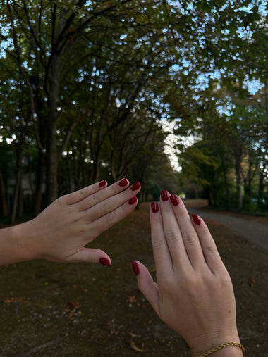 Two hands with red nail polish against a natural background with trees.