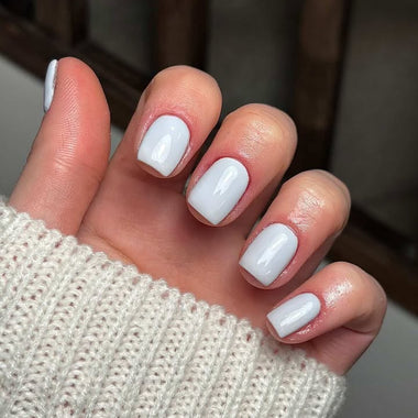 Close-up of a hand with pale grey nail polish wearing a textured beige sleeve.
