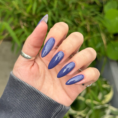 Hand with blue nail polish against a green outdoor background