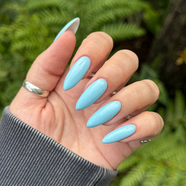 Hand with light blue nail polish against a green leafy background