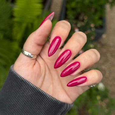 Hand with pink nail polish against a blurred green outdoor background