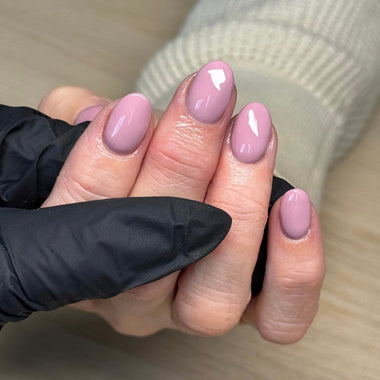 Hand with pink nail polish wearing a black glove on a wooden surface