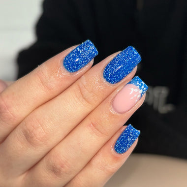 Hand with blue glittery nail polish on a blurred background