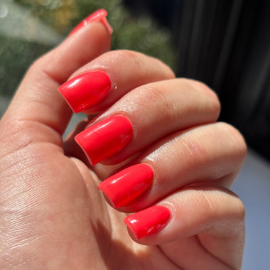 Hand with red nail polish against a blurred outdoor background