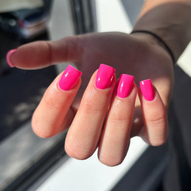 Hand with pink nail polish in front of a window
