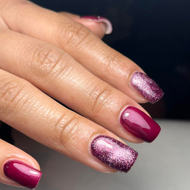 Close-up of a hand with burgundy nails and glittery accents on a dark background