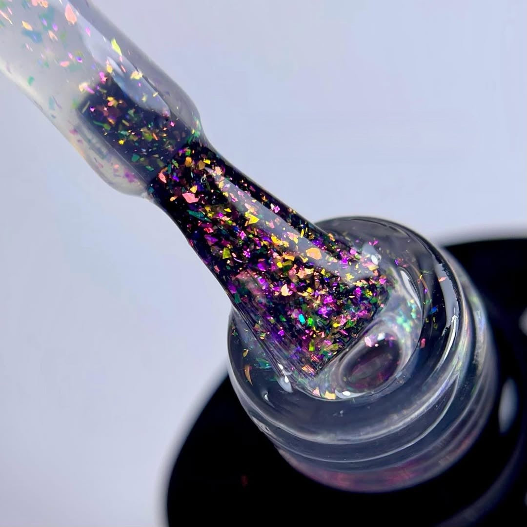 Close-up of a nail polish bottle with glittery polish being applied.