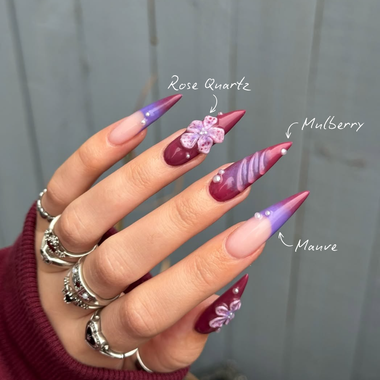 Hand with maroon and purple nail art on a neutral background