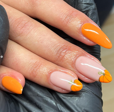 Hand with orange and white pumpkin-themed nail art on a neutral background