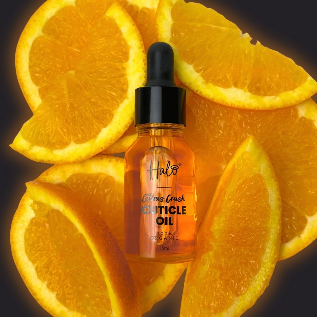 Bottle of Halo Cuticle Oil surrounded by sliced oranges on a dark background