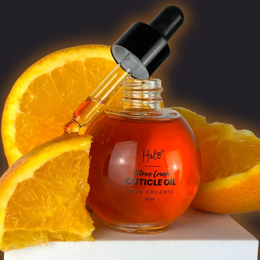 Cuticle oil bottle with dropper surrounded by orange slices on a dark background