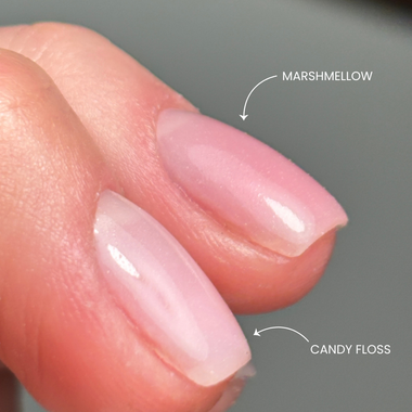 Close-up of a hand with pink nail polish labeled 'Marshmallow' and 'Candy Floss' on a gray background.