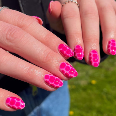 Close-up of hands with bright pink nail polish in a pattern, wearing jeans outdoors.