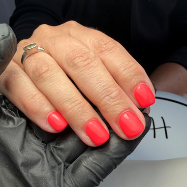 Hand with bright pink nails wearing a black glove against a neutral background