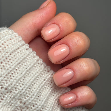 Close-up of a hand with light pink nail polish wearing a textured white sleeve against a gray background