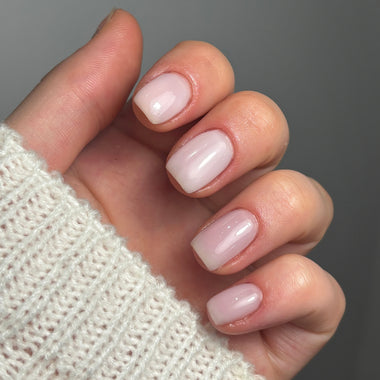 Close-up of a hand with pink nail polish on a neutral background