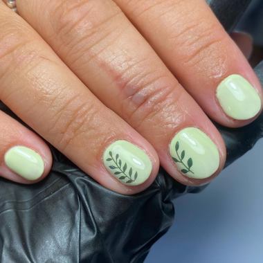 Close-up of a hand with light green nails featuring leaf designs, wearing a black leather jacket.