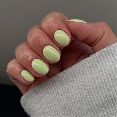 Hand with light green nail polish on a neutral background