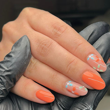 Hand with orange nail polish and floral designs, wearing black gloves.