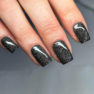 Close-up of a hand with black glittery nail polish on a gray background