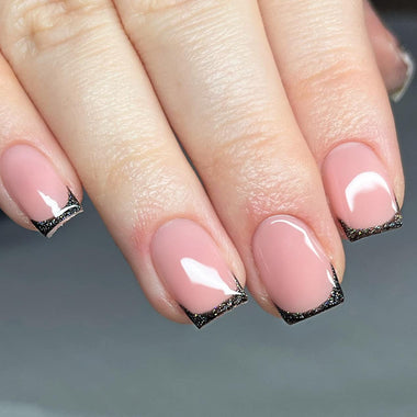 Close-up of a hand with pink nails and black diamond designs on a gray background