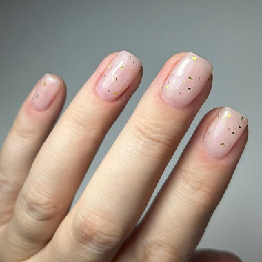 Hand with pink nails with gold flakies on a gray background