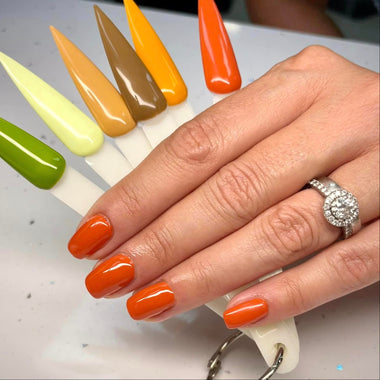 Hand with orange nail polish holding a tray of colorful nail samples.