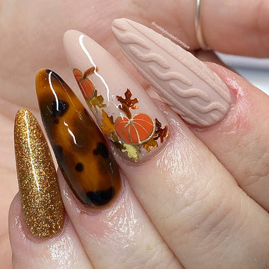 Nail art with autumn theme featuring pumpkins and leaves on a light pink background.