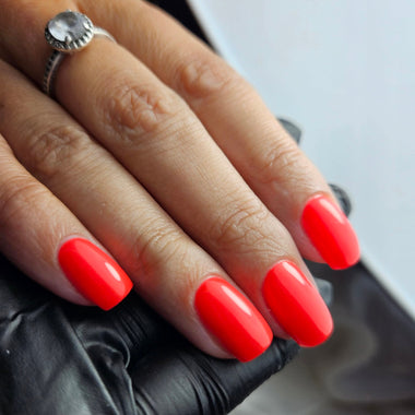Hand with bright orange nails wearing a silver ring on a blurred background
