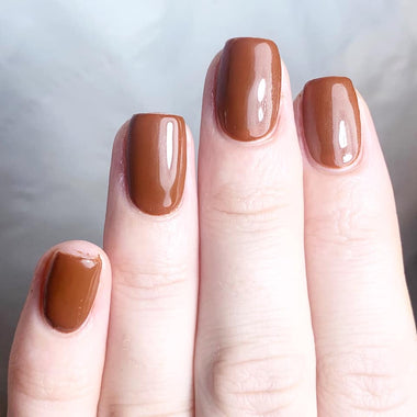 Close-up of a hand with brown nail polish on a neutral background