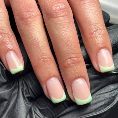 Close-up of hands with light pink and green nail polish on a dark textured background
