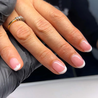 Close-up of a hand with pink nail polish and a gold ring, wearing a black glove.