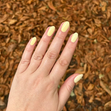 Hand with light yellow nail polish against a background of brown mulch