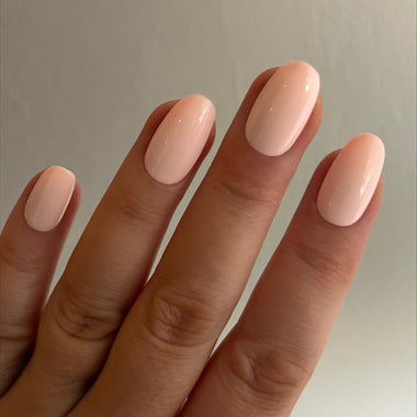 Close-up of a hand with light pink nail polish on a neutral background