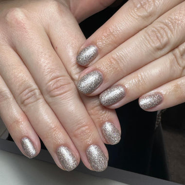 Close-up of hands with silver glittery nail polish on a neutral background